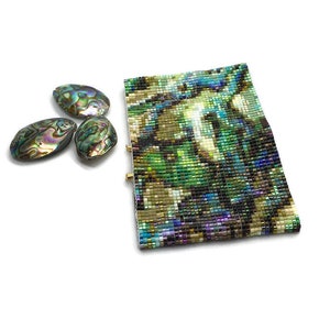 K&ouml;nnte beinhalten: Ein Armband aus Perlen mit einem abstrakten Muster in Gr&uuml;n-, Blau- und Braunt&ouml;nen. Das Armband ist aus kleinen, bunten Perlen gefertigt und hat ein einzigartiges, modernes Design.