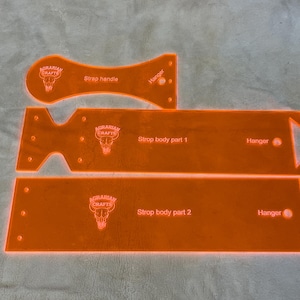 May include: Orange acrylic craft templates with the text "Strap handle", "Strop body part 1", and "Strop body part 2". Each piece has the "Agrarian Crafts" logo and the word "Hanger".