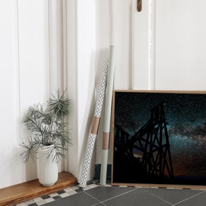 May include: A framed black and white photograph of a large metal structure silhouetted against a night sky filled with stars. The Milky Way is visible in the sky.