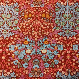 May include: A red fabric with a repeating pattern of blue, pink, and yellow flowers and leaves. The pattern is symmetrical and has a vintage aesthetic.