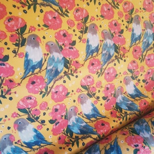 May include: A yellow background with a repeating pattern of pink flowers and blue lovebirds. The lovebirds are perched on branches with green leaves.