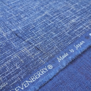 May include: Close-up of blue fabric with a textured weave and a subtle white grid pattern. The text "SEVENBERRY® Made by Japan" is visible along the edge of the fabric.