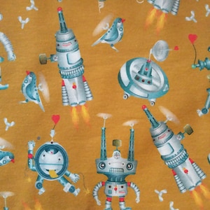 Pode incluir: Um tecido amarelo mostarda com um padrão repetitivo de robôs, pássaros e discos voadores. Os robôs são prateados e azuis com várias formas e tamanhos. Os pássaros são azuis e brancos com um design simples. Os discos voadores são prateados e têm uma forma redonda com uma cúpula no topo.