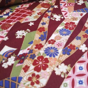 May include: Red fabric with a repeating pattern of white, pink, blue, and gold ribbons with floral designs. The fabric has a textured, woven look.