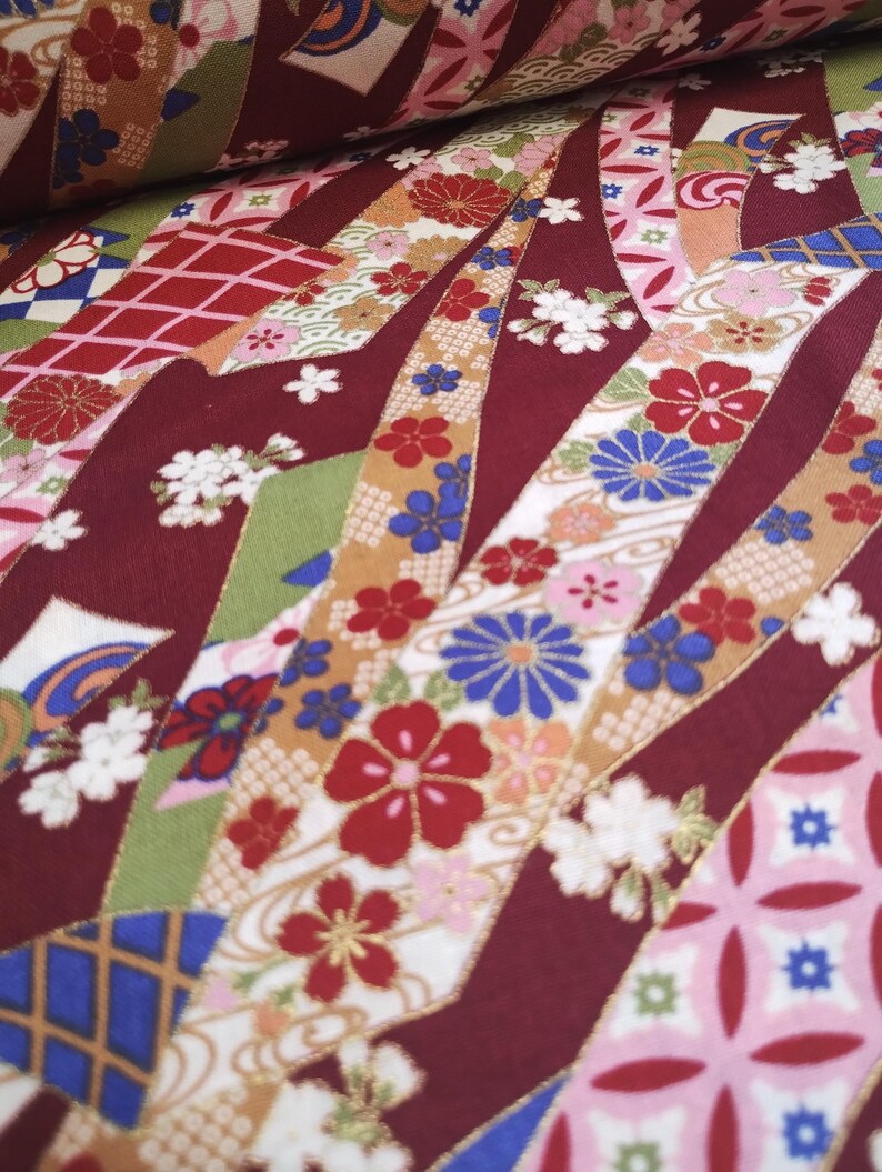 May include: Red fabric with a repeating pattern of white, pink, blue, and gold ribbons with floral designs. The fabric has a textured, woven look.