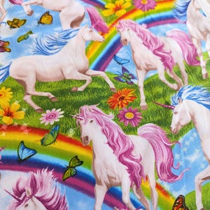 Könnte beinhalten: Stoffmuster mit weißen Einhörnern mit rosa und blauen Mähnen und Schweifen, vor dem Hintergrund von Regenbogen, Schmetterlingen, Blumen und grünem Gras. Das Design hat ein skurriles, Fantasy-Thema.