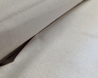 May include: Close-up of a roll of natural-colored canvas fabric. The fabric has a slightly textured surface with visible weave and small flecks. The canvas is rolled, showing the layers and folds of the material.