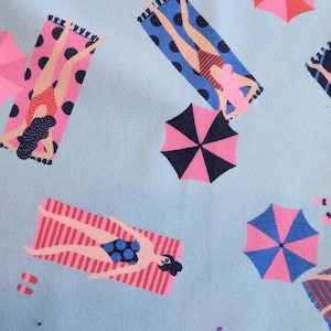 May include: A light blue pattern featuring illustrations of people sunbathing on beach towels, with pink and blue umbrellas. The beach towels have polka dots and stripes. The people are wearing swimsuits. The overall theme is summer and beach.