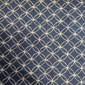 May include: A close-up of navy blue fabric featuring a repeating pattern of interlocking circles in a light beige hue. The circles form a geometric design, giving a textured look.