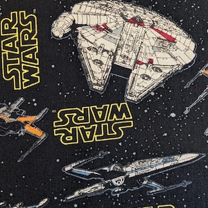 Peut inclure: Un tissu noir avec un motif répétitif de vaisseaux spatiaux Star Wars, incluant le Faucon Millenium et des chasseurs X-wing, entremêlés du logo jaune Star Wars et de petits points blancs représentant des étoiles sur le fond sombre.