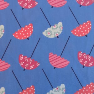 Könnte beinhalten: Ein sich wiederholendes Muster aus bunten Regenschirmen auf blauem Hintergrund. Die Regenschirme haben verschiedene Designs, darunter rosa Streifen, rote Punkte und florale Muster in Weiß und Hellblau. Die Schirmstiele sind dunkelblau.
