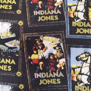 May include: A black and white fabric with a repeating pattern of vintage movie posters featuring Indiana Jones. The posters have a yellow border and the text "Indiana Jones" is written in yellow letters. The posters feature images of people and horses.