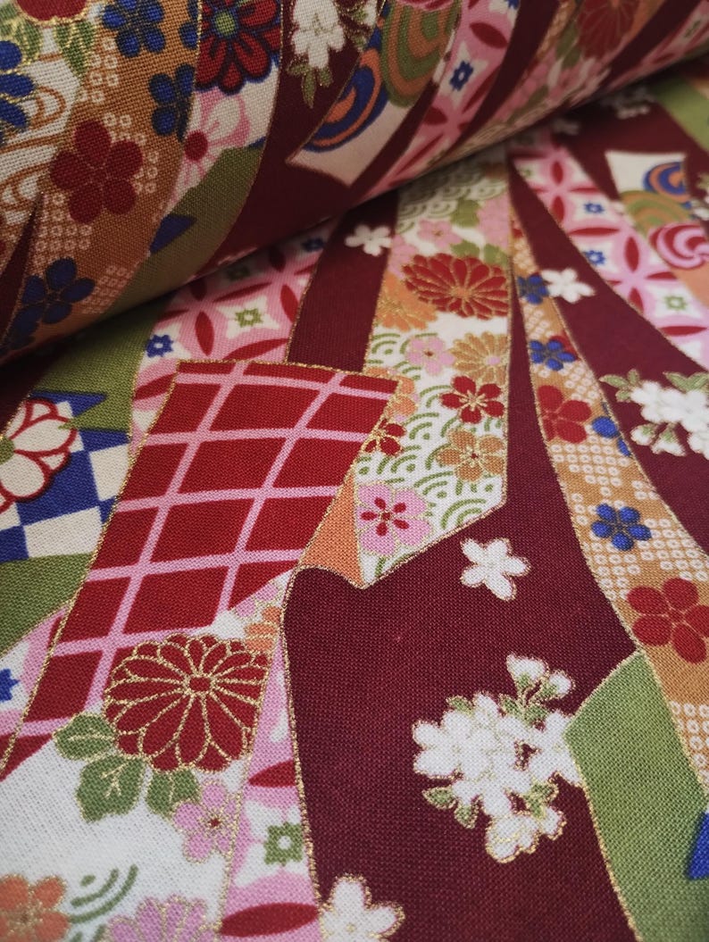 May include: Close-up of a fabric with a colourful Japanese-inspired pattern. The fabric features a variety of flowers, geometric shapes, and gold accents. The fabric is a mix of red, pink, white, green, and gold.