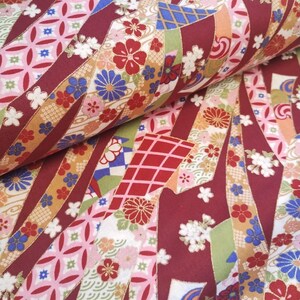 May include: Red fabric with a repeating pattern of colourful ribbons, flowers, and geometric shapes. The fabric has a traditional Japanese design.