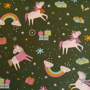 May include: A green fabric with a repeating pattern of pink unicorns, rainbows, stars, snowflakes, and presents. The unicorns are wearing pink scarves and have pink manes.