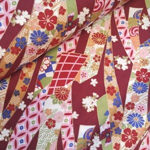 May include: Red, pink, blue and gold patterned fabric with a Japanese-inspired design. The fabric features a variety of floral motifs, geometric shapes and traditional Japanese patterns.