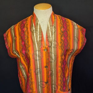May include: A sleeveless, button-up shirt with a colorful geometric pattern in shades of orange, brown, pink, and white. The shirt has a V-neck and two pockets.