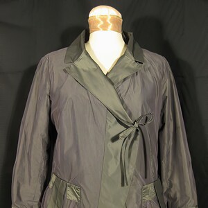 May include: A gray, long-sleeved jacket with a wrap-style closure and a tie at the waist. The jacket has two pockets on the front and a contrasting black collar.