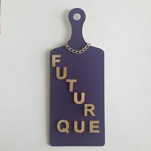May include: A purple wooden cutting board with a handle and a gold chain necklace. The word "FUTURE" is spelled out in gold letters on the board. The board is a decorative item.