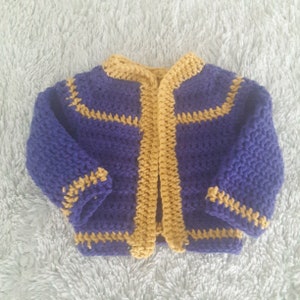 May include: A purple and gold crocheted cardigan with a button closure. The cardigan has a simple design with a contrasting color trim.