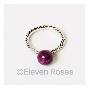 May include: A silver ring with a twisted band and a purple gemstone. The ring is on a white background.