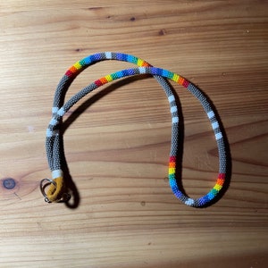 May include: A rainbow beaded lanyard with a grey and white beaded pattern. The lanyard has a brown leather loop and a metal ring.