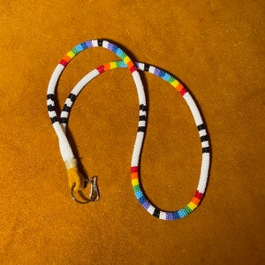 May include: A beaded lanyard with a rainbow pattern and black and white accents. The lanyard has a metal clasp.