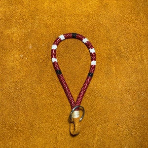 May include: A red, white and black beaded keychain with a silver key ring. The keychain is made of small beads and is about 15 cm long.