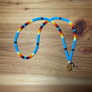 May include: A beaded lanyard with a blue, black, white, orange and red pattern. The lanyard has a brown leather tassel and a metal clip.
