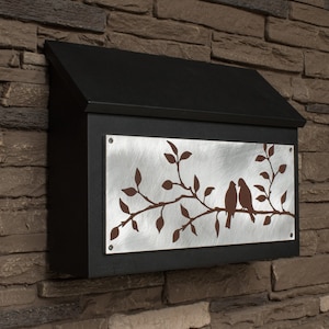 May include: Black metal mailbox with a silver metal panel featuring a cut-out design of two birds perched on a branch with leaves.