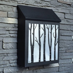 May include: Black metal mailbox with a silver metal panel featuring a cutout design of a forest of trees.