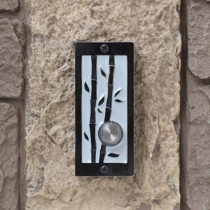 May include: A black doorbell with a white background and a bamboo design. The doorbell has a silver button.