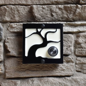 May include: Black doorbell with a white background featuring a stylised tree design. The doorbell button is round and silver.