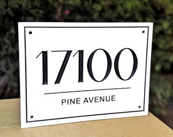 Pode incluir: Uma placa de endereço retangular branca com texto preto. Os números "17100" são exibidos acima das palavras "PINE AVENUE". A placa tem uma borda preta e pequenos orifícios em cada canto.