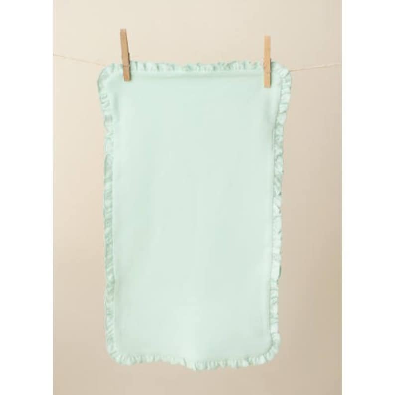 May include: A light green baby blanket with a ruffled edge. The blanket is hanging on a clothesline with wooden clothespins.