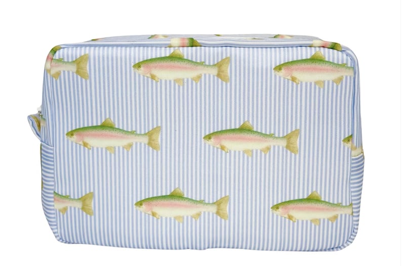 May include: A rectangular cosmetic bag with a blue and white striped background. The bag is decorated with illustrations of rainbow trout. The fish are green, pink, and yellow. The bag has a zipper closure and a small side pocket.