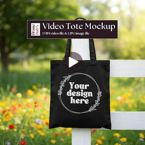 May include: Black tote bag with a white floral design and the text "Your design here." The bag hangs on a white fence against a backdrop of colorful flowers and greenery. The image includes the text "Video Tote Mockup."