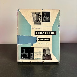 May include: A vintage book titled "Furniture for Interiors" by Mario Dal Fabbro. The cover features a blue and cream color scheme with architectural illustrations and the publisher's name, Reinhold. The book is displayed on a dark surface.