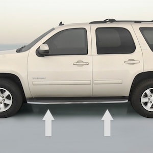 May include: Side view of a white SUV with a silver running board. The vehicle has a black roof rack and tinted windows. The word "YUKON" is visible on the side of the vehicle.