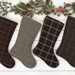 May include: Four Christmas stockings with hanging loops, each featuring a distinct pattern: a red and black plaid, a grey and black glen check, a brown and black plaid with blue accents, and a dark brown fabric with a subtle black grid pattern.