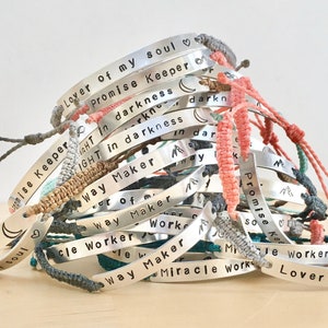 a large order off handmade metal silver bar bracelets. bracelets stamped with motivational text. each custom made with a personalised engraving and has a woven adjustable wristband in mixed colours. bracelets customised with emojis.