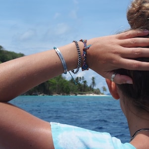 photo of personalised bracelet being worn. hand-stamped custom engraved bar bracelet modelled by woman looking out to beach island.