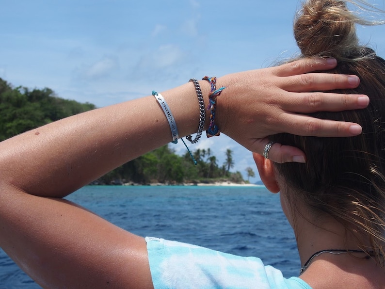 photo of personalised bracelet being worn. hand-stamped custom engraved bar bracelet modelled by woman looking out to beach island.
