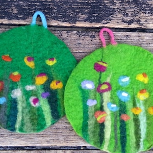 Könnte beinhalten: Zwei grüne Filz-Topflappen mit bunten Blumendesigns. Die Topflappen haben eine Schlaufe zum Aufhängen.