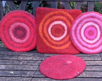 May include: Five round wool cushions with concentric circles in shades of red, pink, yellow, and orange. The cushions are arranged on a wooden bench.