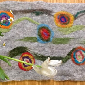 May include: A gray felt rug with a colorful abstract design. The design features multiple circles with concentric rings of different colors, including red, orange, yellow, green, blue, and purple. The rug is decorated with green and gray lines that resemble flowing water.
