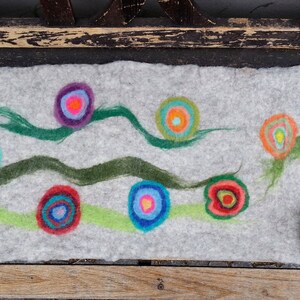 May include: A gray felt pillow with a colorful abstract design. The design features green, blue, red, orange, yellow, and purple circles with concentric rings. The circles are arranged in a random pattern on the pillow.