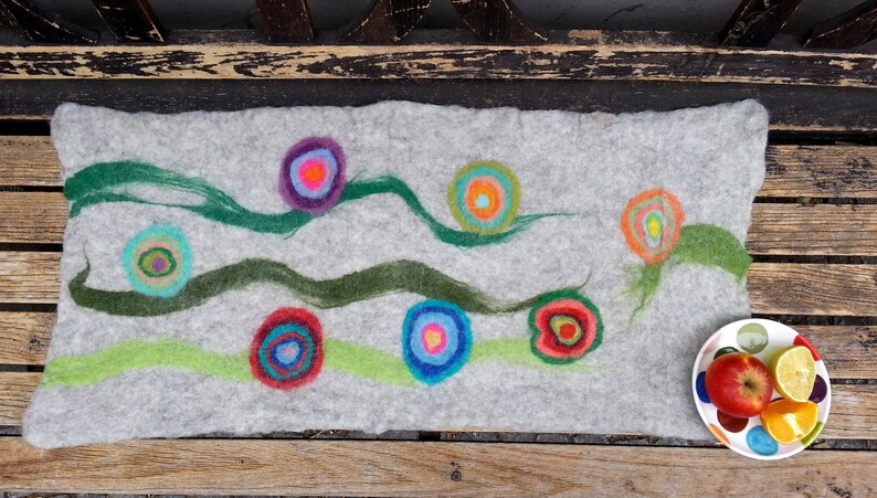 May include: A gray felt pillow with a colorful abstract design. The design features green, blue, red, orange, yellow, and purple circles with concentric rings. The circles are arranged in a random pattern on the pillow.