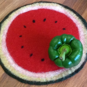 Pode incluir: Um descanso de panela redondo de feltro com a forma de melancia com uma pimenta verde em cima. O descanso de panela tem um centro vermelho com sementes pretas e um anel exterior branco e verde.