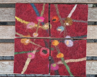 May include: Four square coasters with a deep red background. Each coaster features colorful, abstract designs with lines and circular shapes in various colors like yellow, blue, and pink. The coasters are made of a textured material.